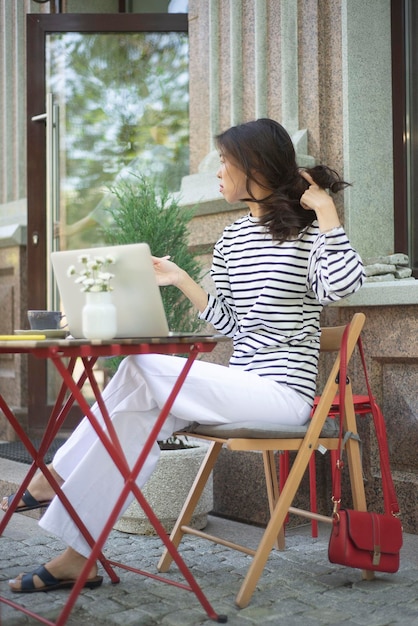 A freelance girl works at a computer in an outdoor cafe