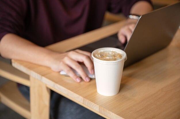 Freelance man working with laptop and coffee cup on wooden table in cafe