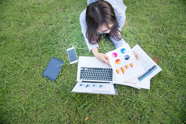 Freelance Met behulp van laptop slimme tablet en smartphone vast op groen grasveld lezen spreadsheet.