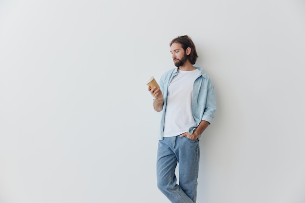 Freelance millennial man met een baard die koffie drinkt uit een gerecyclede beker in stijlvolle hipster kleding witte T-shirt blauwe spijkerbroek en shirt op een witte achtergrond