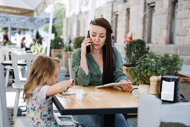 Freelance parents busy working mom with cell phone and tablet working in street cafe with baby