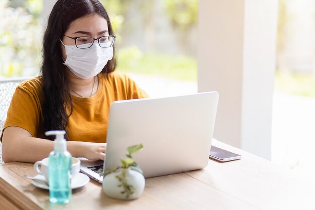 Femmina di affari della gente freelance che indossa la maschera protettiva che lavora casuale con il computer portatile nella caffetteria come lo sfondo