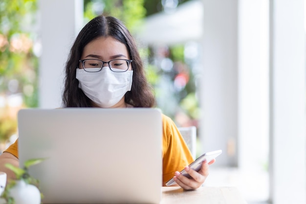 Freelance people business female wearing protective mask casual and writing message on smartphone working with laptop computer ,working from home,Concept of Prevention of the spread of COVID-19 virus