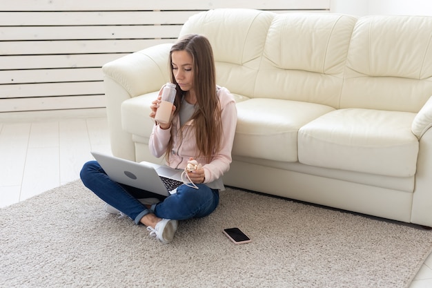 Photo freelance and people concept - young woman sitting on floor and working at laptop.