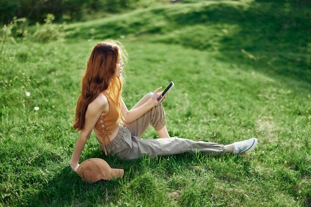 Freelance student werkt aan de telefoon en zit in de zomer buiten op groen gras mobiel en internet buiten de stad