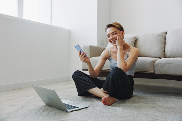 Freelance vrouw met laptop en telefoon werkt vanuit huis zittend op de vloer in haar huiskleren met een kort kapsel gratis kopieerruimte Foto van hoge kwaliteit