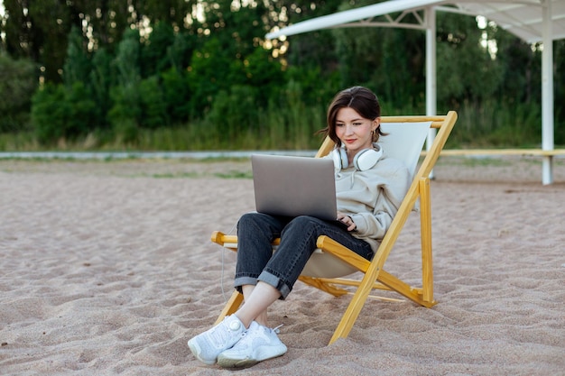 Freelance vrouw zittend op een ligstoel en werkend op de computer aan de oever van het meer