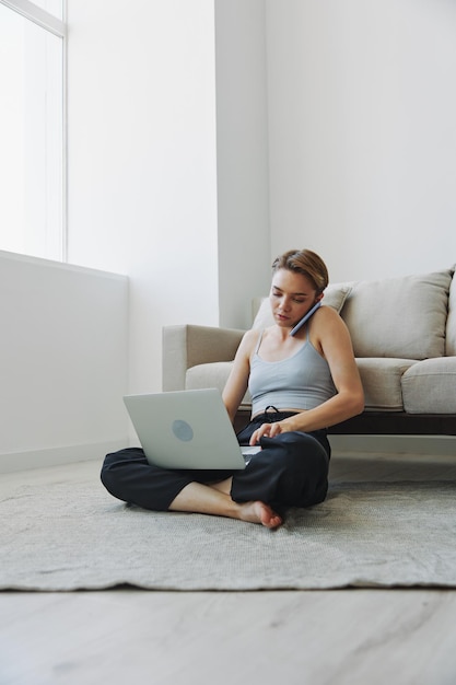 Freelance woman with laptop and phone works from home sitting on the floor in her home clothes with a short haircut free copy space High quality photo