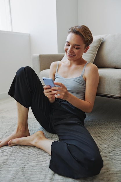 Freelance woman with laptop and phone works from home sitting on the floor in her home clothes with a short haircut free copy space