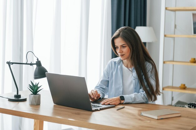 Freelance worker is sitting by table with laptop young\
beautiful woman is home alone in domestic room