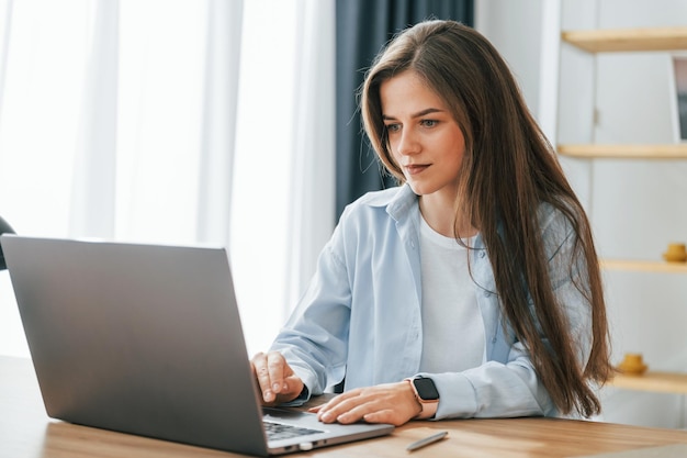 Freelance worker is sitting by table with laptop young\
beautiful woman is home alone in domestic room