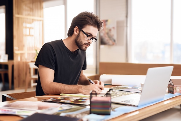 Freelancer bebaarde man notities maken op laptop.