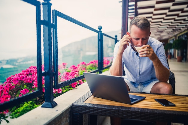 Freelancer concept Succesvolle jonge man zakenman werkt op een laptopcomputer zittend op het terras koffie drinken en praten aan de telefoon