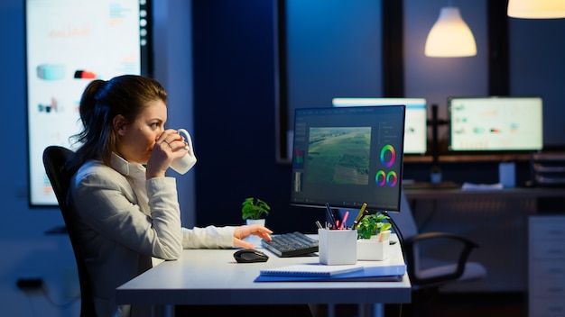 Photo freelancer content creator working overtime to respect deadline sitting at desk in start-up business office. woman videographer editing audio film montage on professional laptop at midnight.