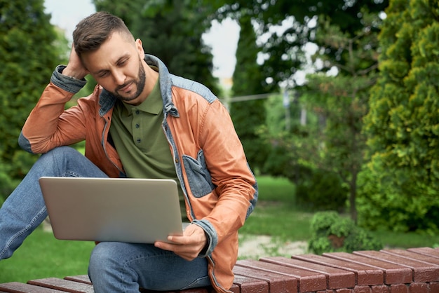 Freelancer die aan laptop op houten bank in tuin werkt