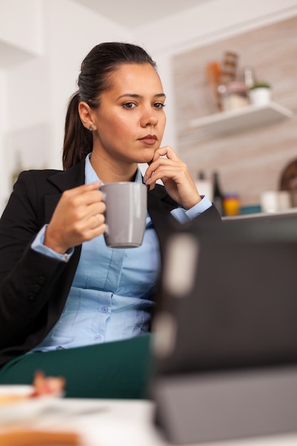 Freelancer drinking coffee in the morning on table top during breakfast using tablet computer