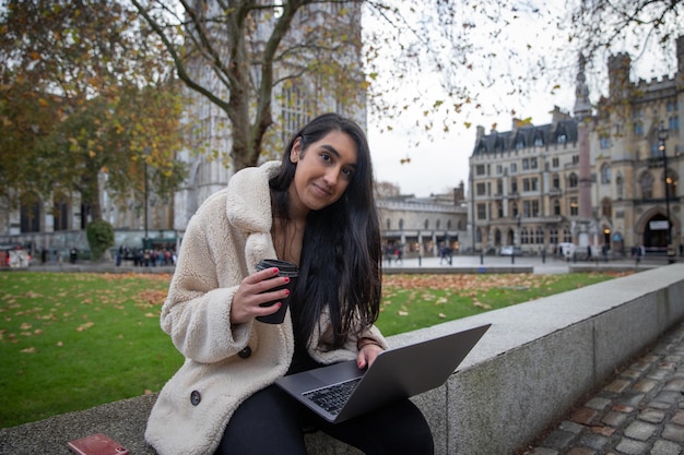 A freelancer girl works with her laptop outdoors while drinking coffee