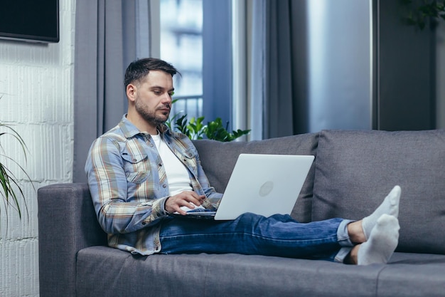 Freelancer Handsome young man working on laptop at home Lying on the couch in home clothes