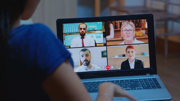 Freelancer having video conference at night with team sitting on couch using laptop. Remote worker discussing at online meeting, consulting with colleagues using videocall and webcam working from home