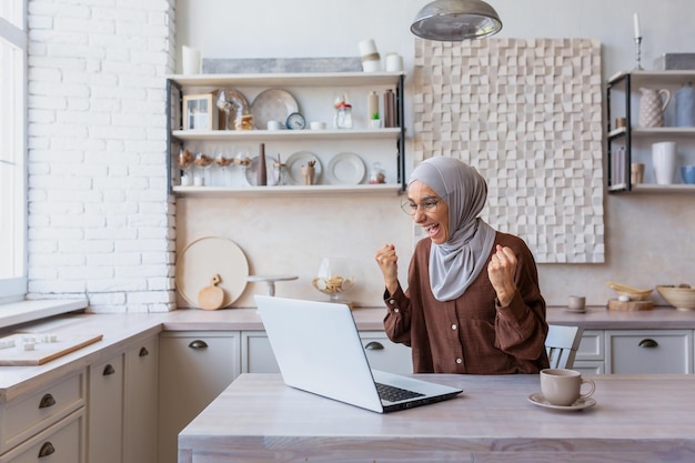 Freelancer in hijab working on laptop remotely from home woman received good news and good news