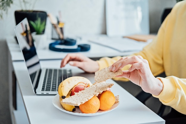 Freelancer jonge vrouw die gezond voedsel eet wanneer ze thuis werkt vrouw die gezonde graansnacks eet