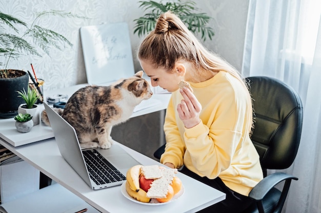 Freelancer jonge vrouw die gezond voedsel eet wanneer ze thuis werkt Vrouw die gezonde graansnacks eet