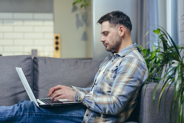 Freelancer Knappe jonge man aan het werk op laptop thuis Liggend op de bank in huiskleding