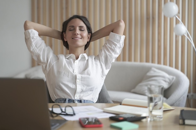 Freelancer lady sitting in front of laptop in relaxed position eyes closed and hands behind head