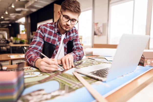 Freelancer man drawing on plan at laptop sitting at desk.