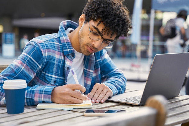 ラップトップ コンピューターを屋外で作業するノートを作るフリーランサーの男。学生の勉強、オンライン教育