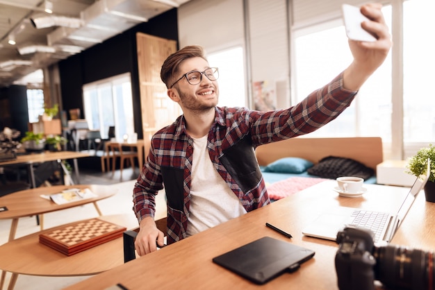 Freelancer man taking selfie at laptop sitting at desk.