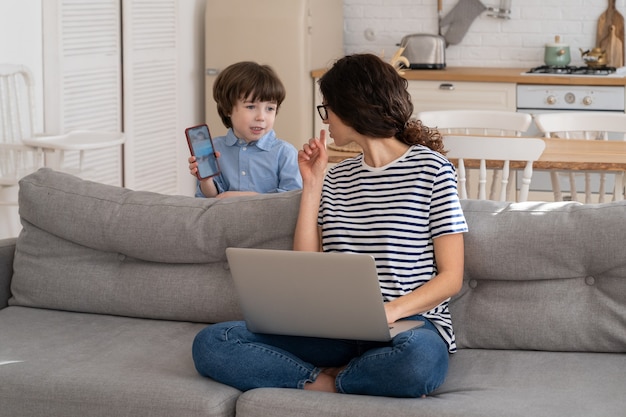 Freelancer moeder bezig met laptop thuis tijdens lockdown, luidruchtig kind leidt af om aandacht te vragen.