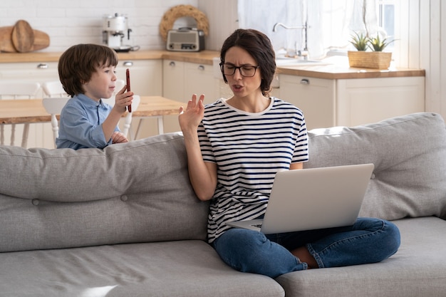 Freelancer moeder bezig met laptop thuis tijdens lockdown, luidruchtig kind leidt af om aandacht te vragen.