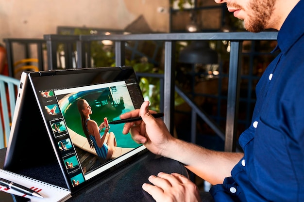 Freelancer retoucher man works on convertible laptop computer with photo editing software using