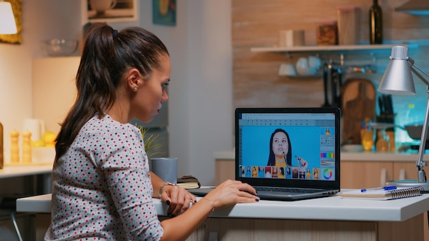 Photo freelancer retoucher woman working on laptop computer with photo editing software. professional graphic editor retouching photos of a client during night time in home office on performance pc.