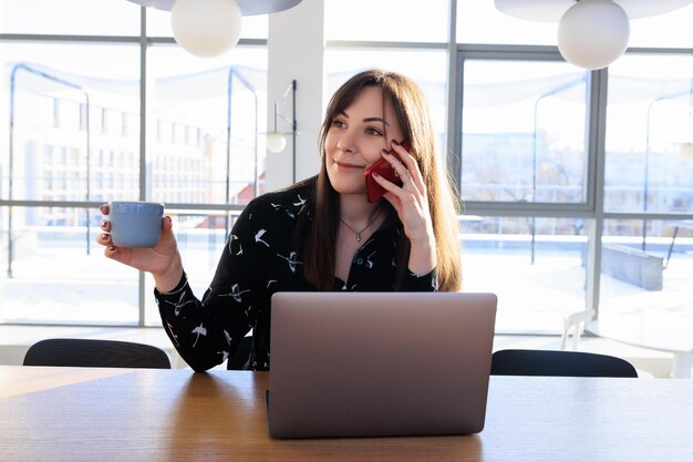 Freelancer's werkdag een jonge vrouw die aan de telefoon praat en koffie drinkt in een café