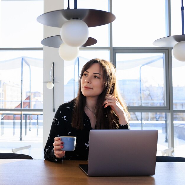 Freelancer's werkdag - een jonge vrouw drinkt koffie en werkt op een laptop in een café