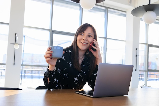 Freelancer's working day brunette talking on the phone and drinking coffee in a cafeBeautiful and stylish businesswoman