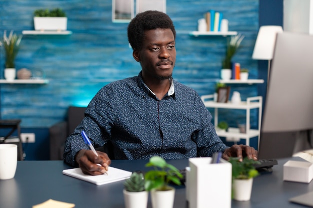 Freelancer taking notes on notebook looking at computer