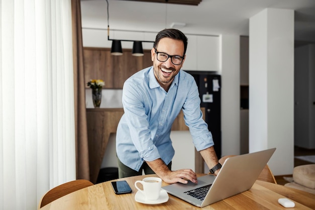 A freelancer uses laptop at home while smiling at the camera