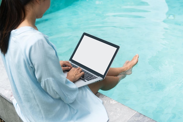 Freelancer using laptop working remotely near swimming pool\
young asian traveler woman working on computer during her summer\
holiday technology and lifestyle concept closeup copy space