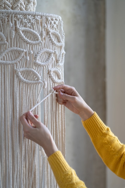 Freelancer vrouw bezig met half afgewerkt macramé stuk, weeft lampenkap voor kroonluchter