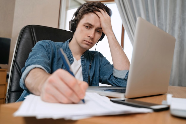 Foto libero professionista che indossa le cuffie che lavora in remoto con il laptop