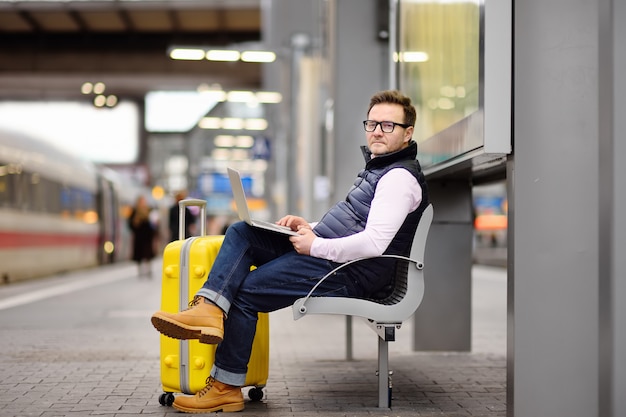 Freelancer werkt met een laptop in een treinstation terwijl hij wacht op transport