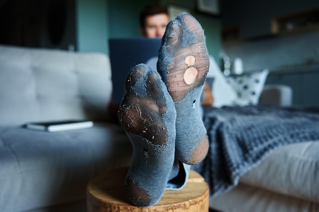 Freelancer werkt vanuit huis man in lekkende sokken met behulp van laptop en rustend op de bank