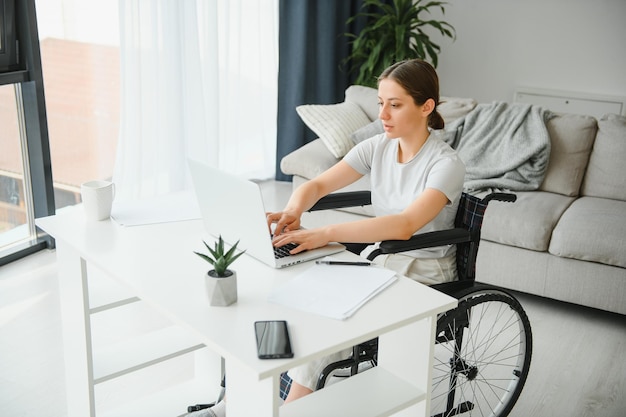 Freelancer in wheelchair using laptop near notebook and papers on table