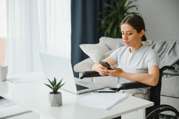 Freelancer in wheelchair using laptop near notebook and papers on table