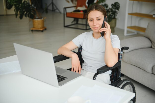 Freelancer in wheelchair using laptop near notebook and papers on table