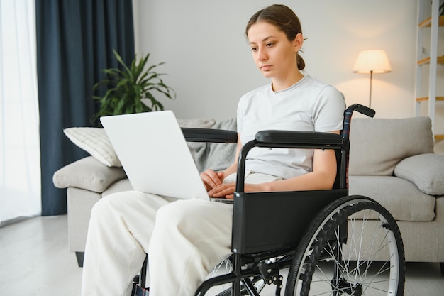 Freelancer in wheelchair using laptop near notebook and papers on table