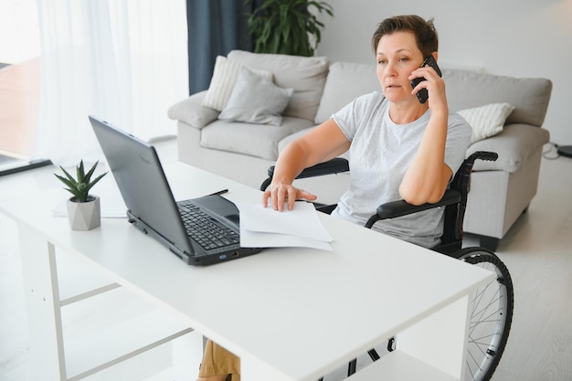 Freelancer in wheelchair using laptop near notebook and papers on table